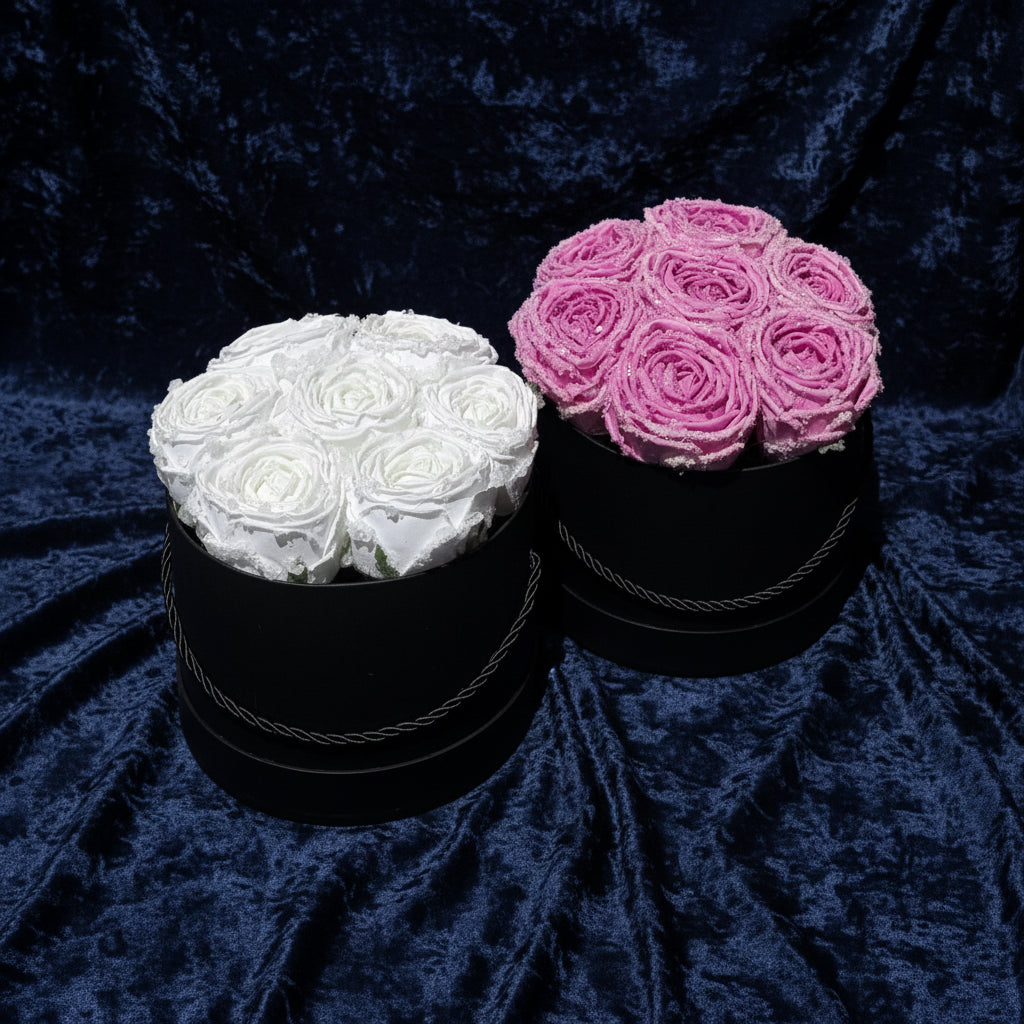 Two black round boxes with white and pink rose bouquets on a light gray background