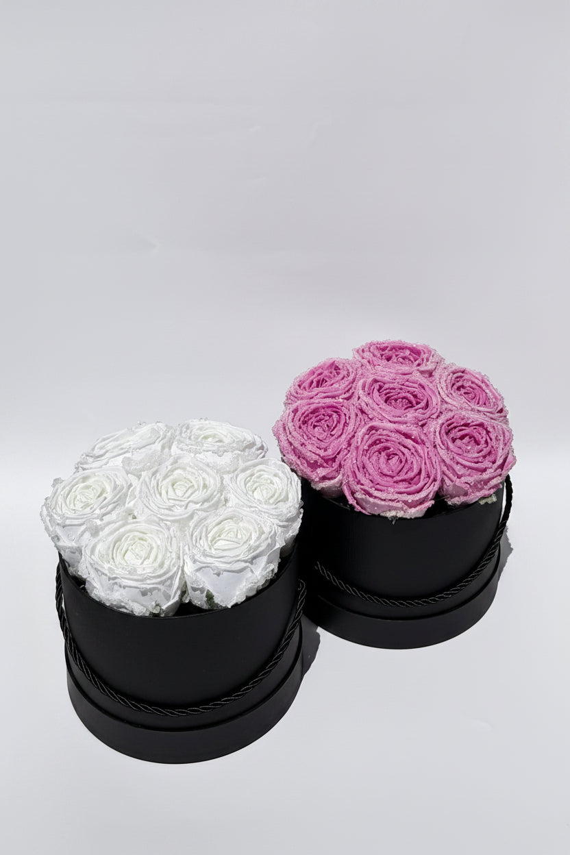 Two black round boxes with white and pink roses on a light gray background