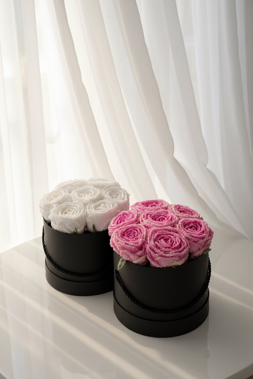 Two black round boxes with white and pink roses on a dark background