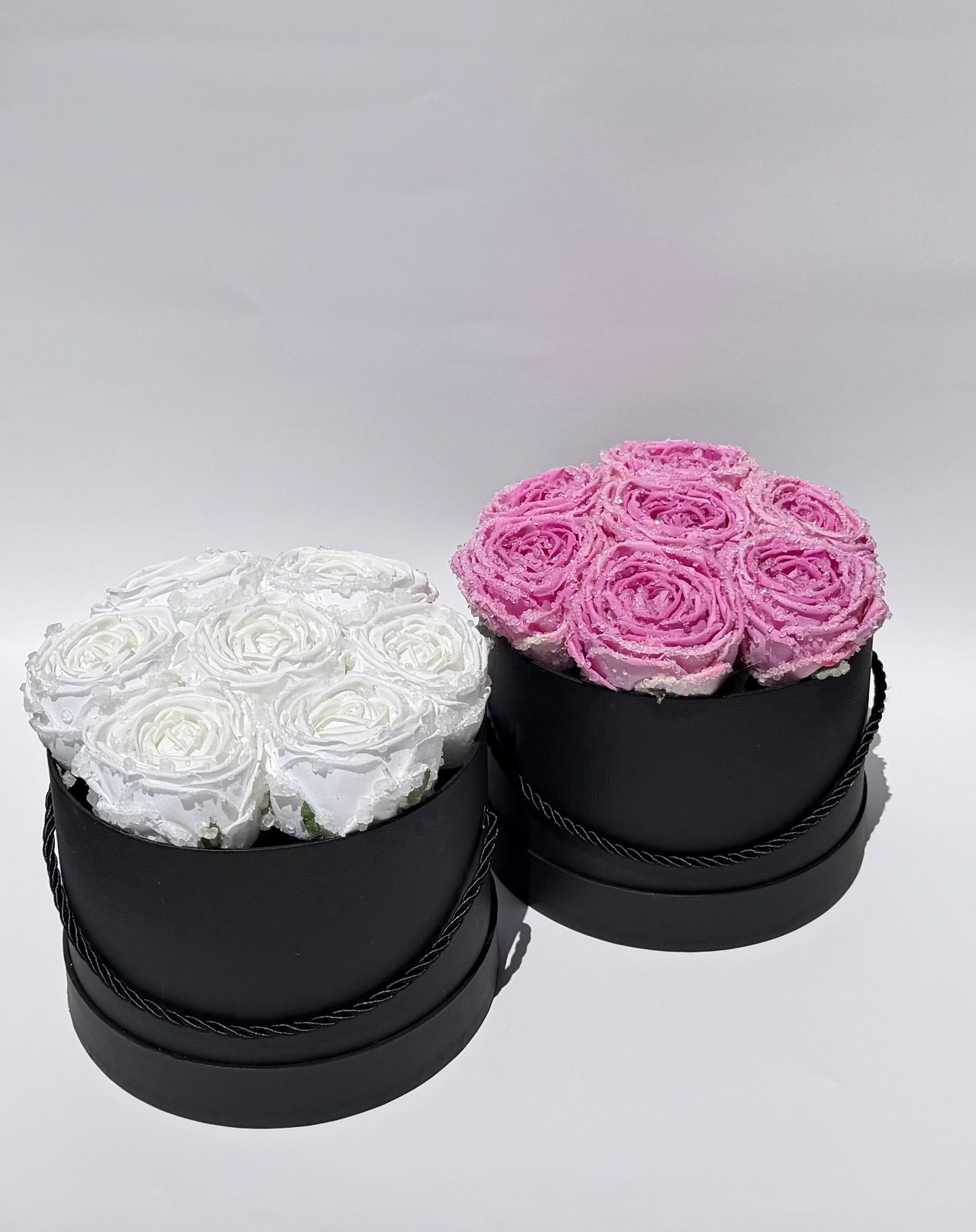 Two black round boxes with white and pink roses on a light gray background