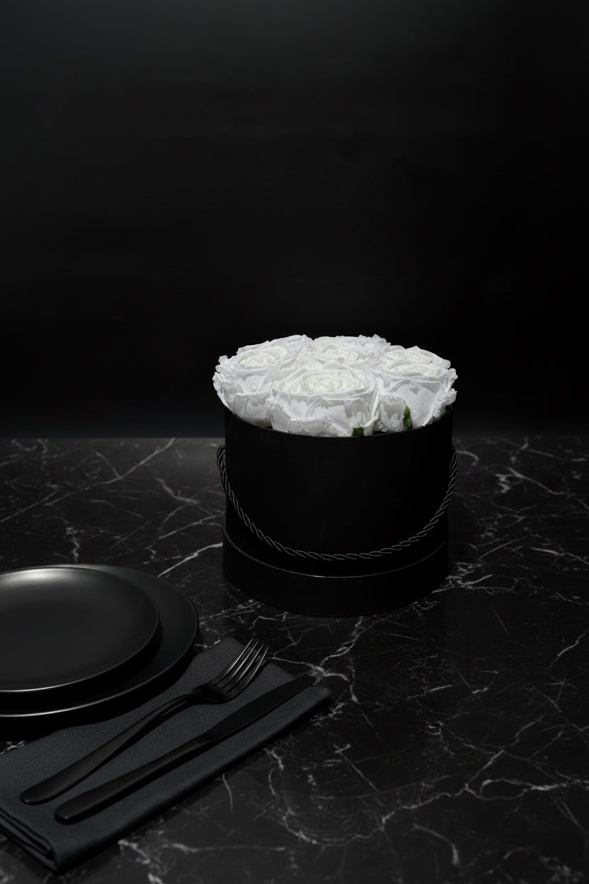 Black box with white flowers on a dark marble surface with black plates and cutlery.