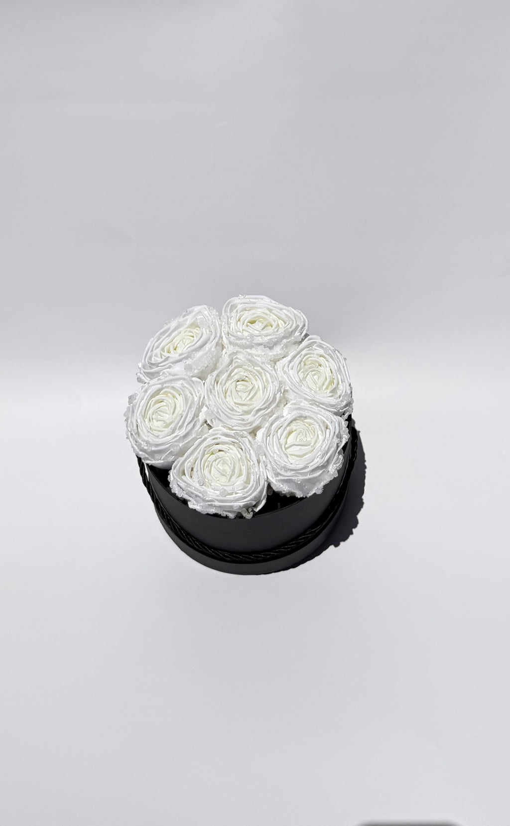 White roses in a black round container on a light gray background