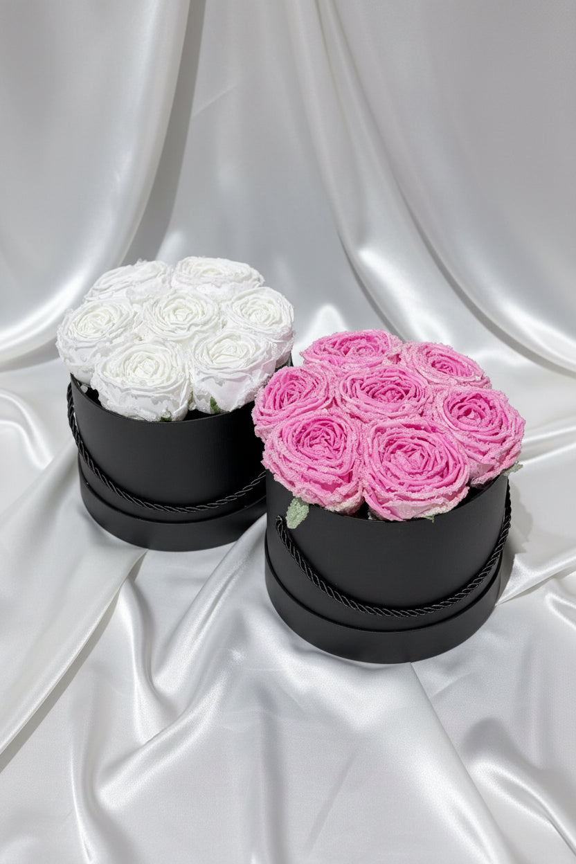 Two black round boxes with white and pink roses on a dark background