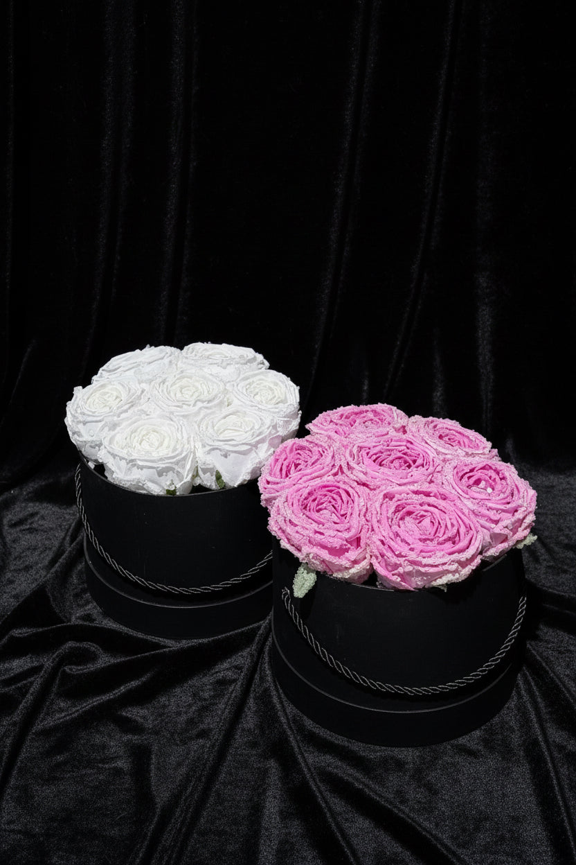 Two black round boxes with white and pink roses on a black background
